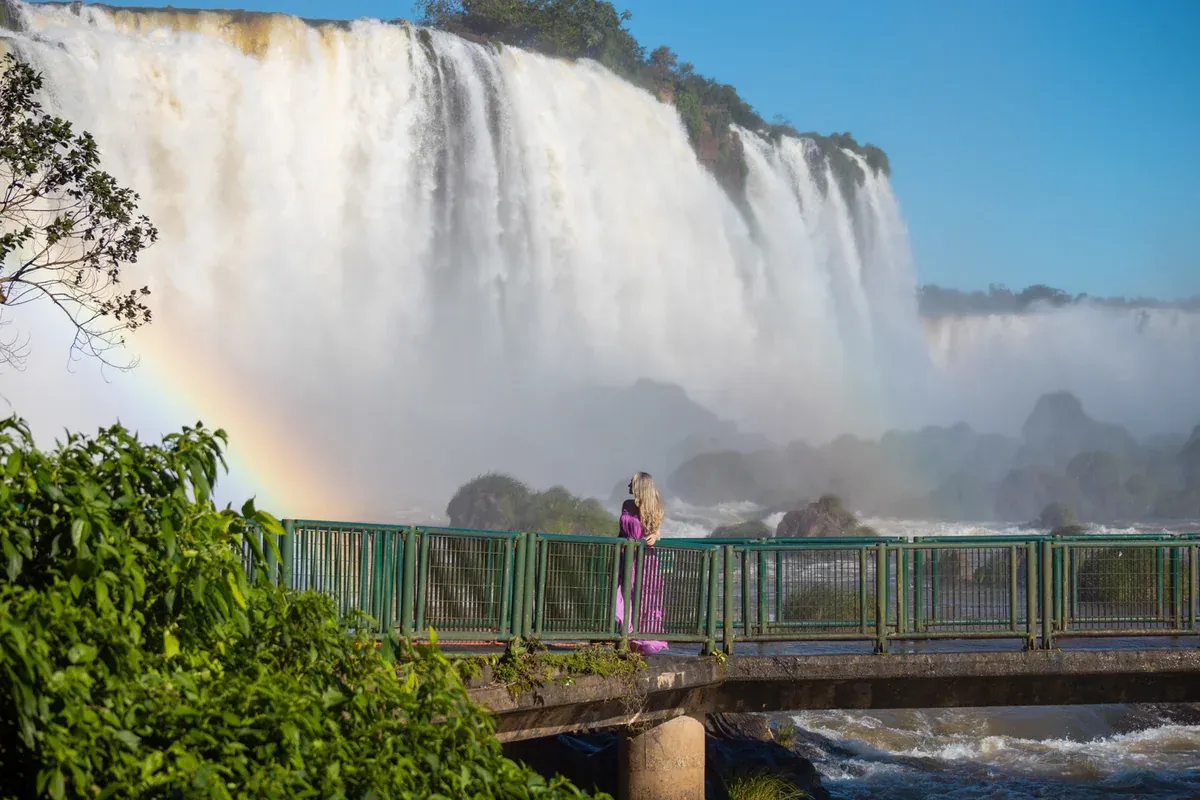 Ensaio de Rafael Guimarães com visitante na passarela diante das Cataratas do Iguaçu e um arco-íris